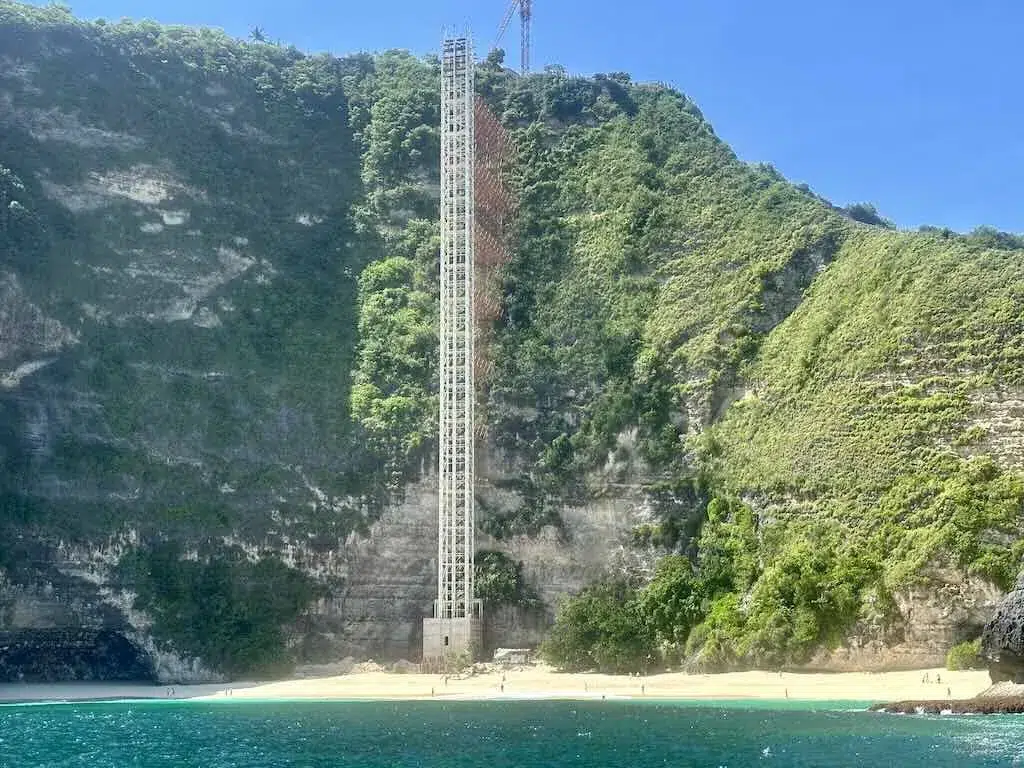 La cage d'ascenseur inachevée plantée dans la falaise de Kelingking Beach, vue depuis un bateau, avec la plage de sable blanc à son pied